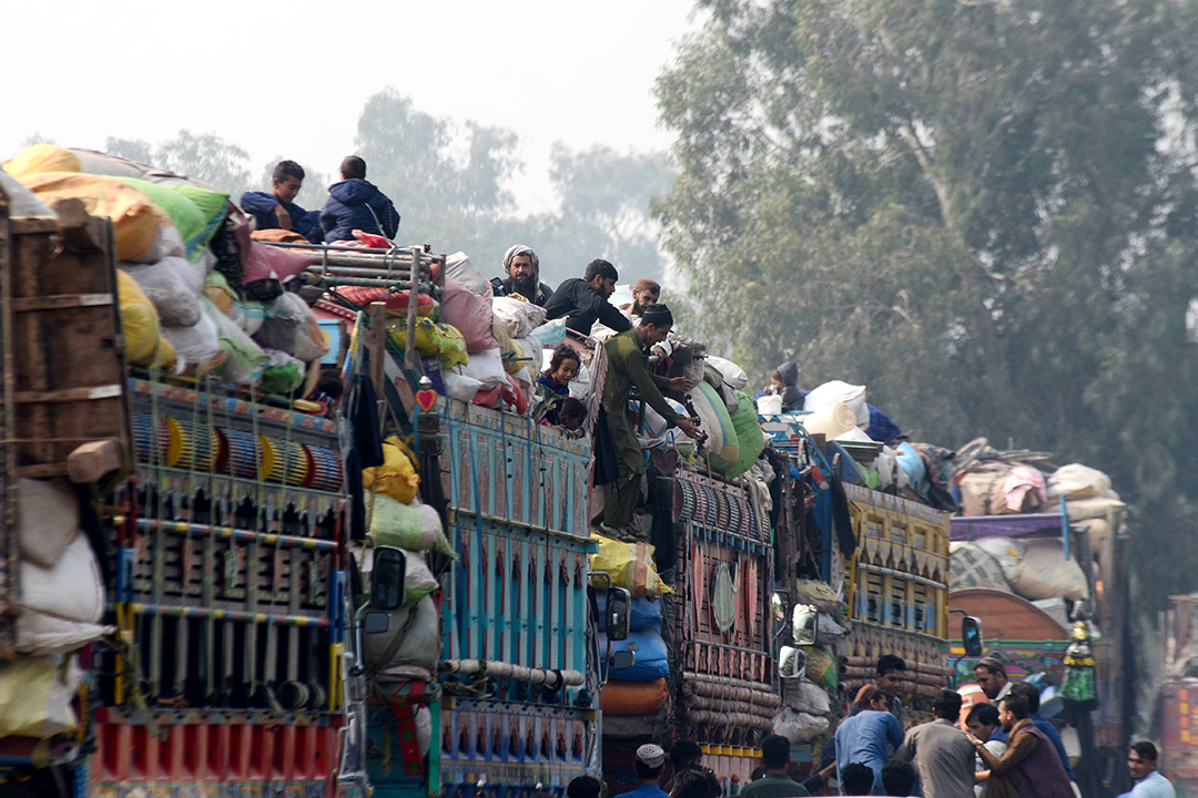 Groups of Afghan refugees sit atop large trucks at a border crossing between Pakistan and Afghanistan.
