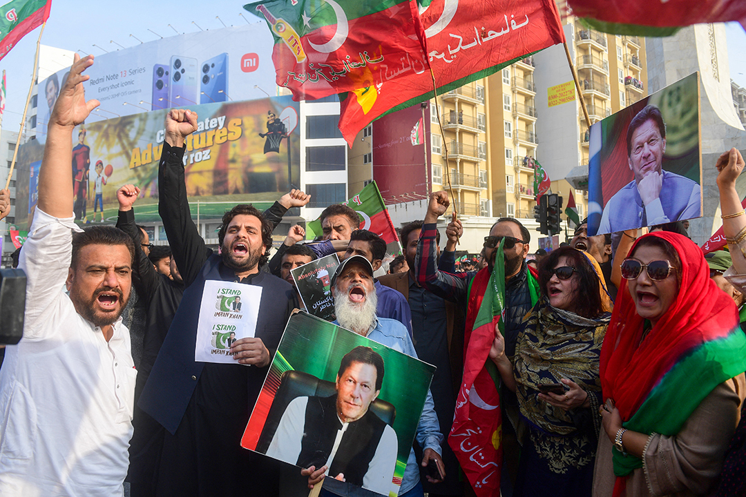 Protestors raise their hands while holding images of former Pakistani Prime Minister Imran Khan and flags representing his party.
