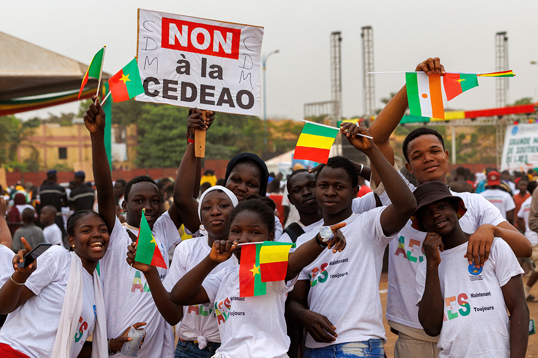 A group of protestors hold the flags of Burkina Faso, Mali, and Niger and signs in support of ECOWAS withdrawal.
