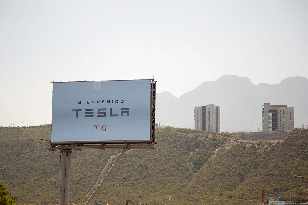 A Tesla billboard foregrounds an arid landscape.