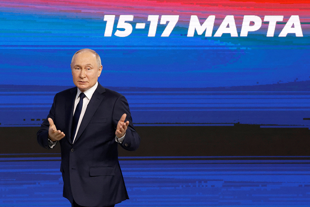 Russian President Vladimir Putin stands in front of a screen reading, 