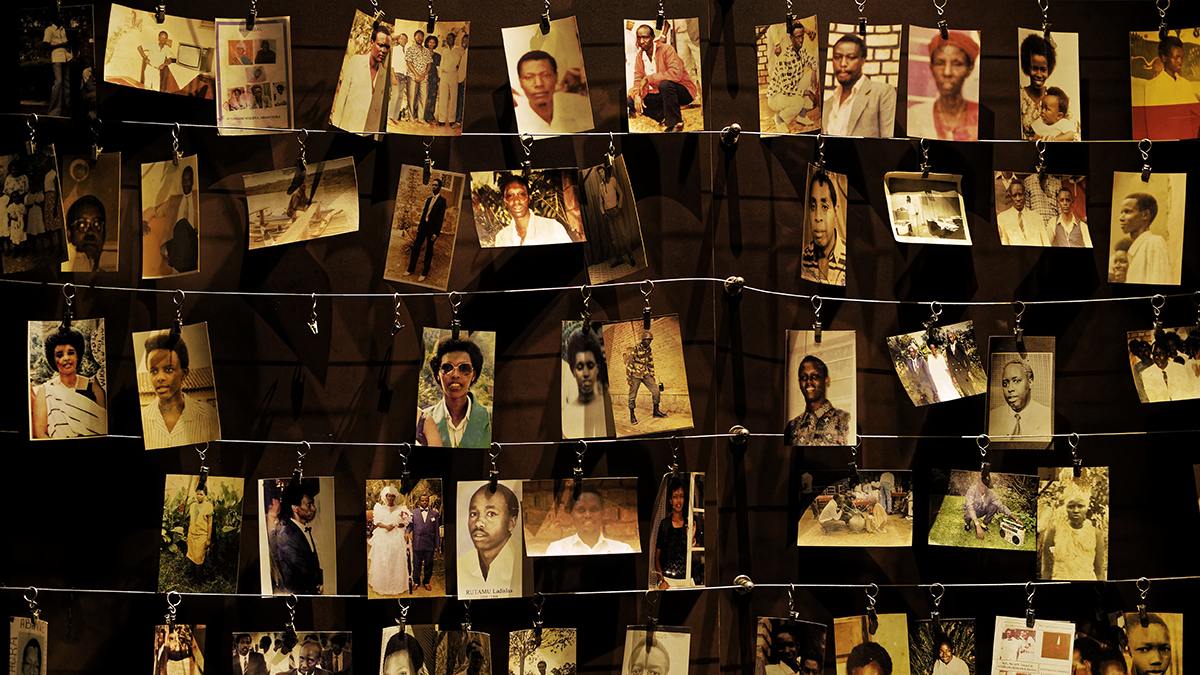 Several photographs of people that were lost in the genocide hang on hooks from wires in five rows.