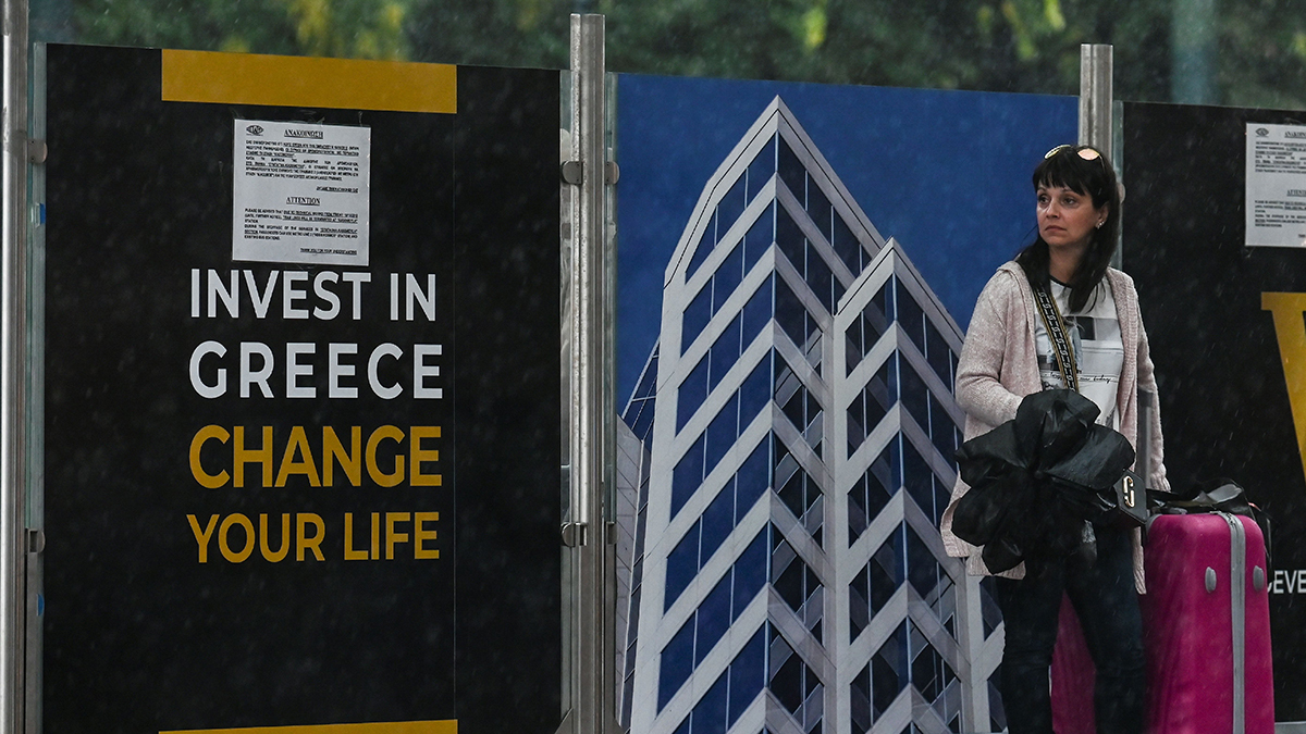 A woman stands at a tram station decorated with Golden Visa advertisements in Athens, Greece.