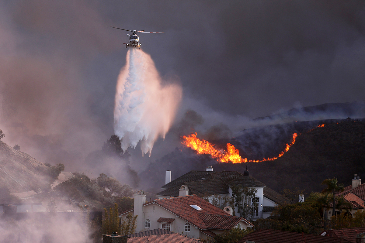  A helicopter drops water around homes threatened by the wind-driven Palisades Fire in Pacific Palisades, California, January 7, 2025. 