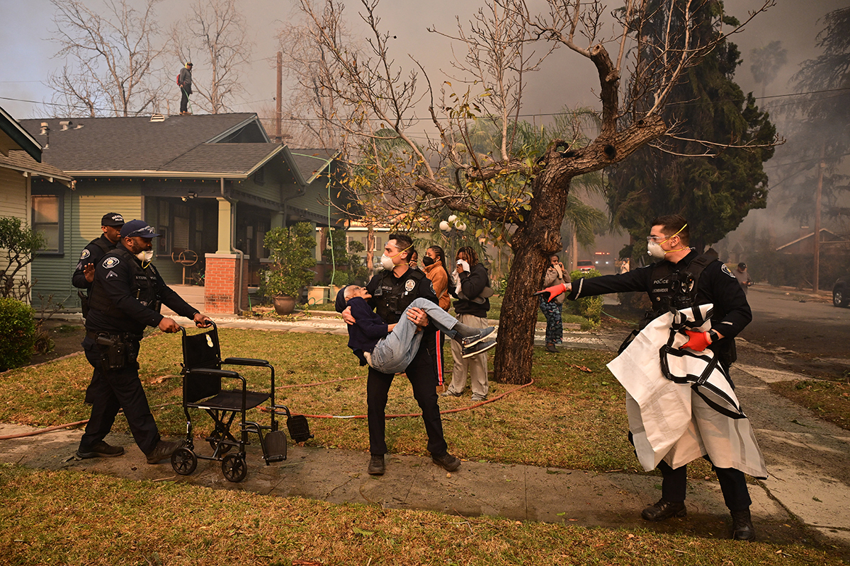 Police officers remove an elderly resident from her home during the Eaton Fire in Altadena, California, on January 8, 2025.