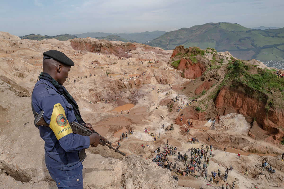 An armed policeman watches over a mine and those working in it.