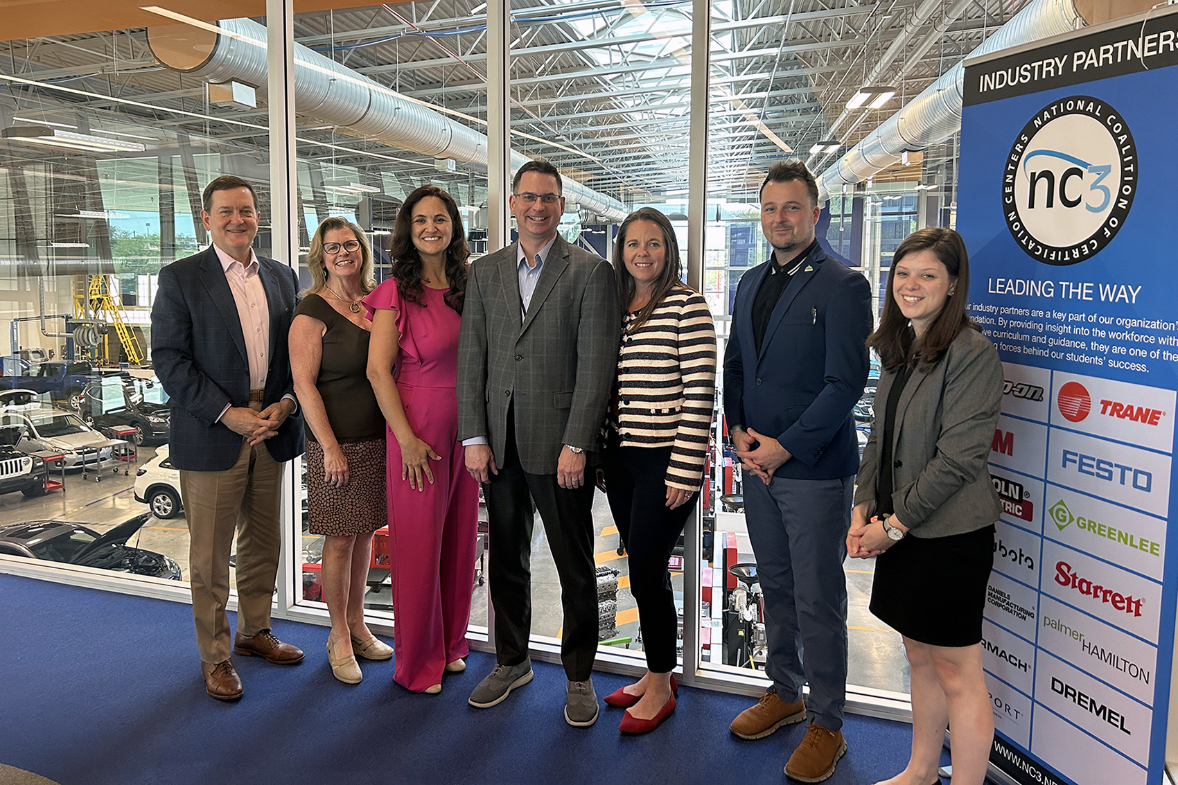 The seven representatives from RealEcon and Pima Community College standing in a row overlooking the college's autoshop.