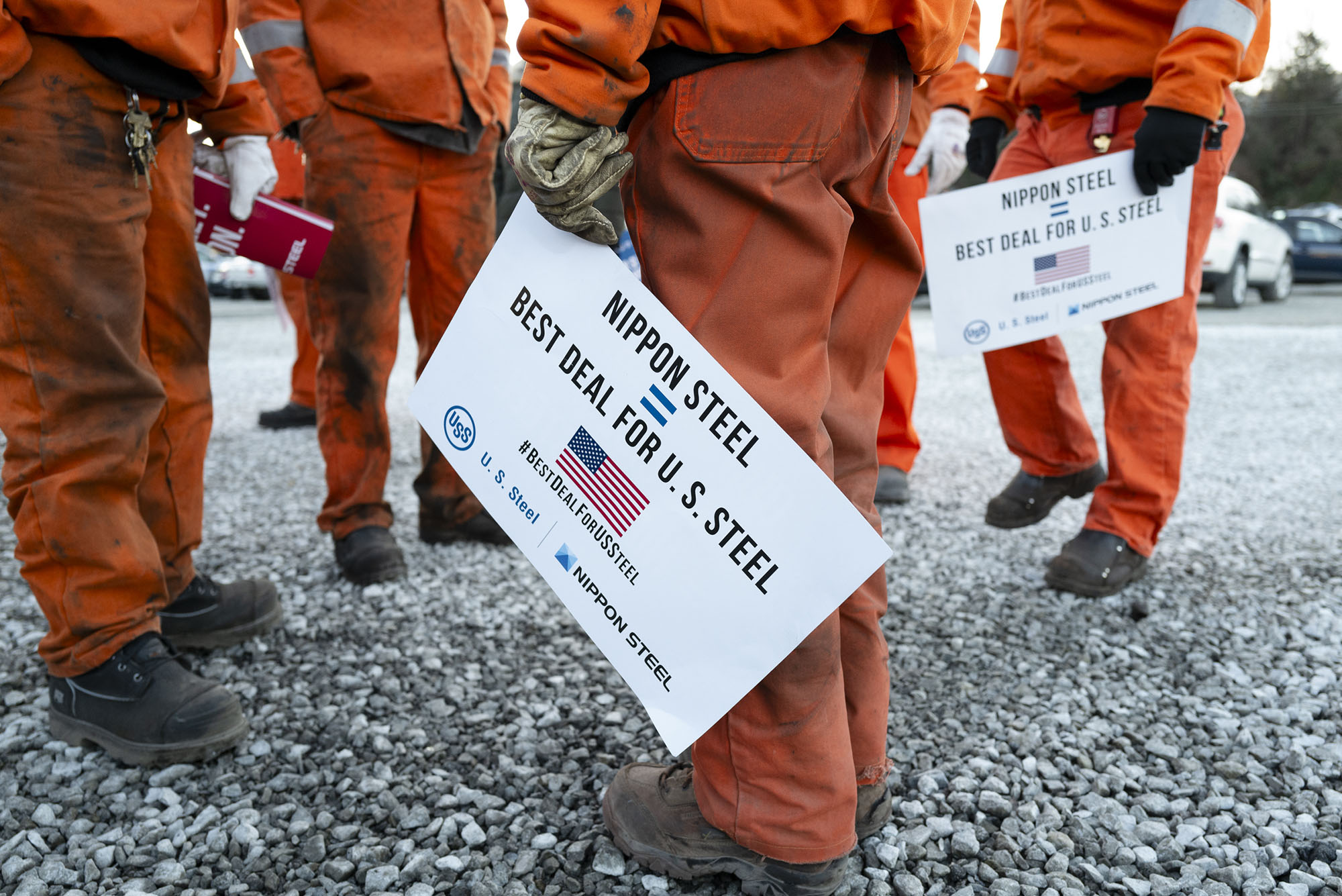 The legs and boots of four workers, all in orange, two carrying protest signs that read 