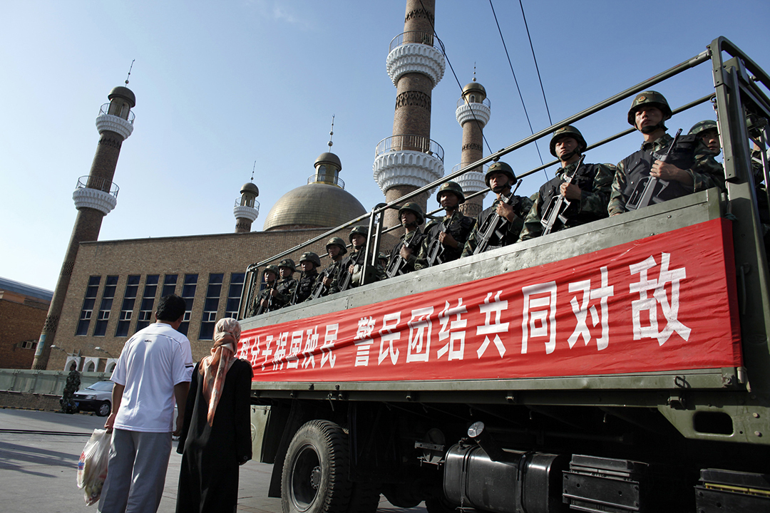 An ethnic Uighur couple waits as a truck loaded with Chinese paramilitary police is driven out of a temporary base position outside a main mosque in Urumqi.