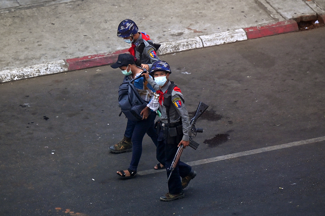 Two helmeted police officers escort a journalist as they arrest him, walking down the street.