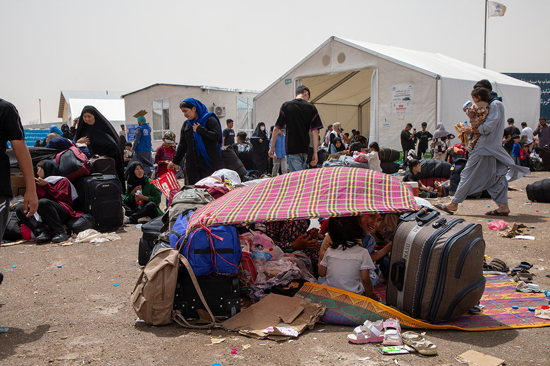 Image show deported Afghan families from Iran sitting in a makeshift shelter.