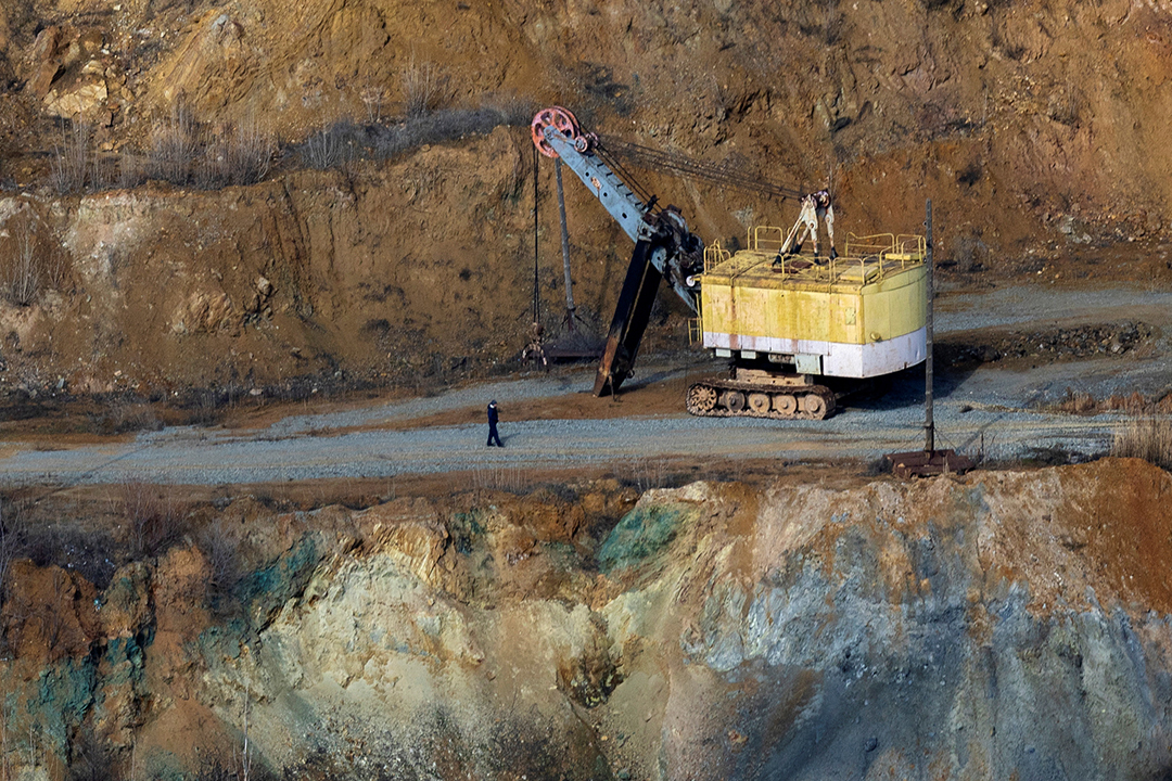 A view of the open pit mine in Ukraine shows a worker walking next to a large piece of machinery on a gravel road.